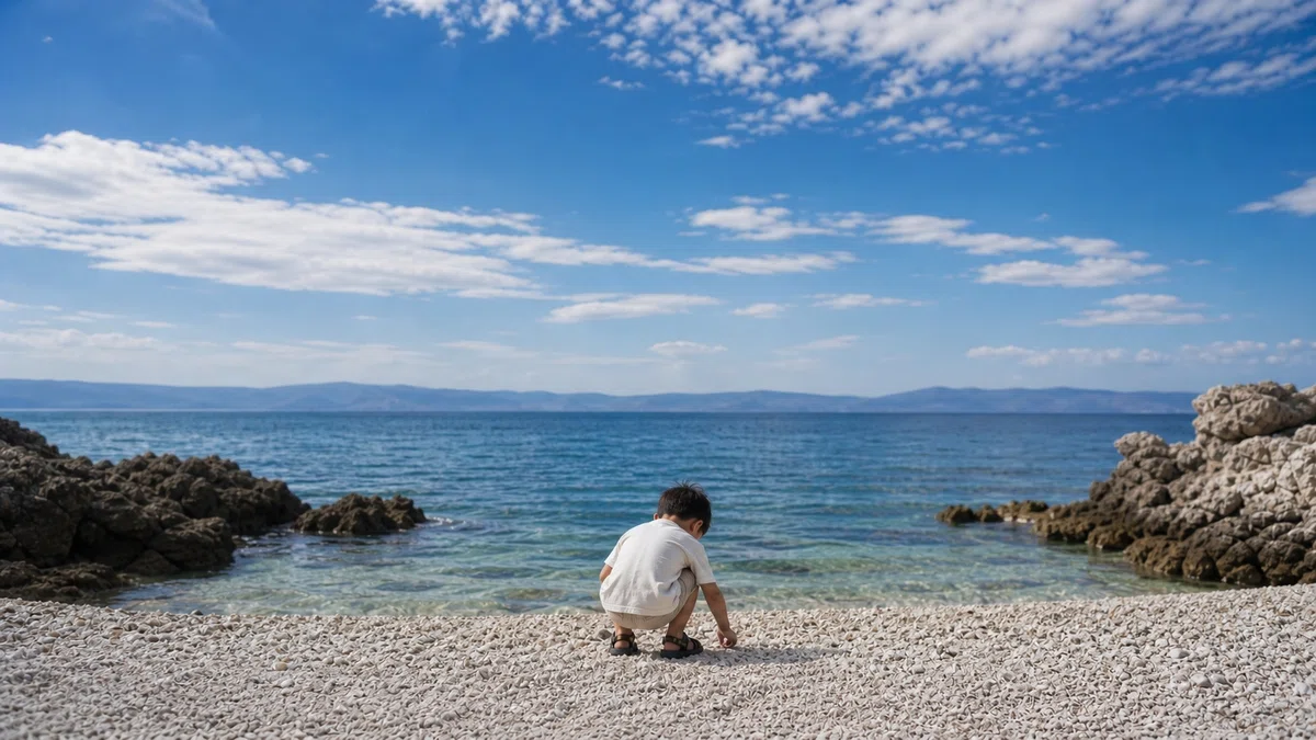 海辺でゴミを拾う子どもの後ろ姿。海外での体験を通して自然の大切さに気づいた小学生の姿と、親が世界を見せることで育つ子どもの感性を表現したアトムズアカデミーのイメージ。