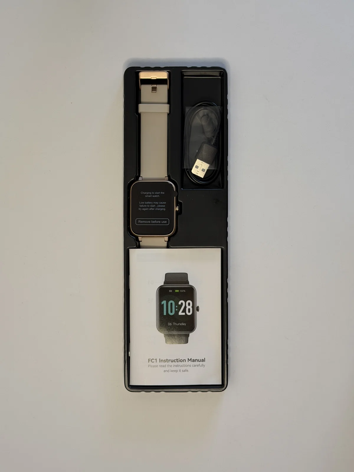 GRV FC1スマートウォッチの箱と付属品。ベージュゴールドの本体、ベルト、充電ケーブル、説明書が入っている。