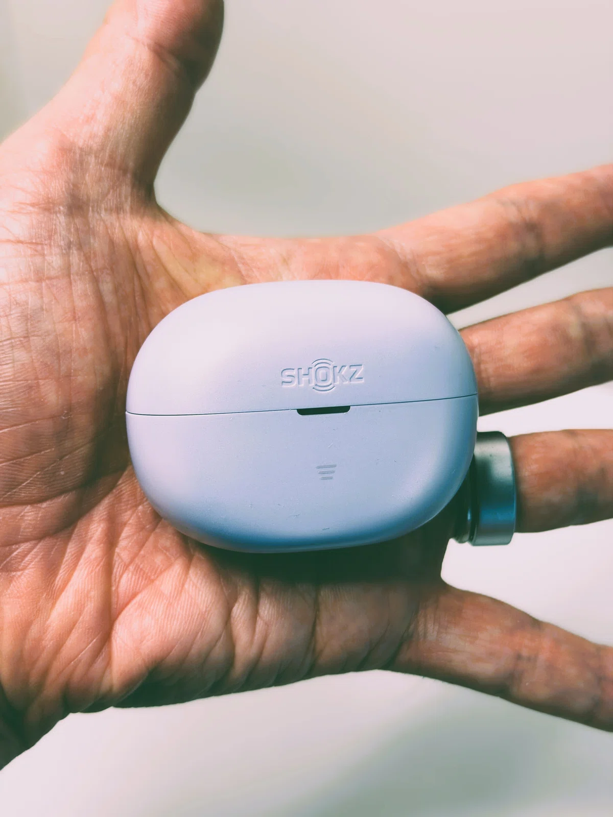 Shokz OpenDots Air デイブレイクパープル。耳に挟んで使うイヤーカフ型イヤホンのケースを手に持っている写真。