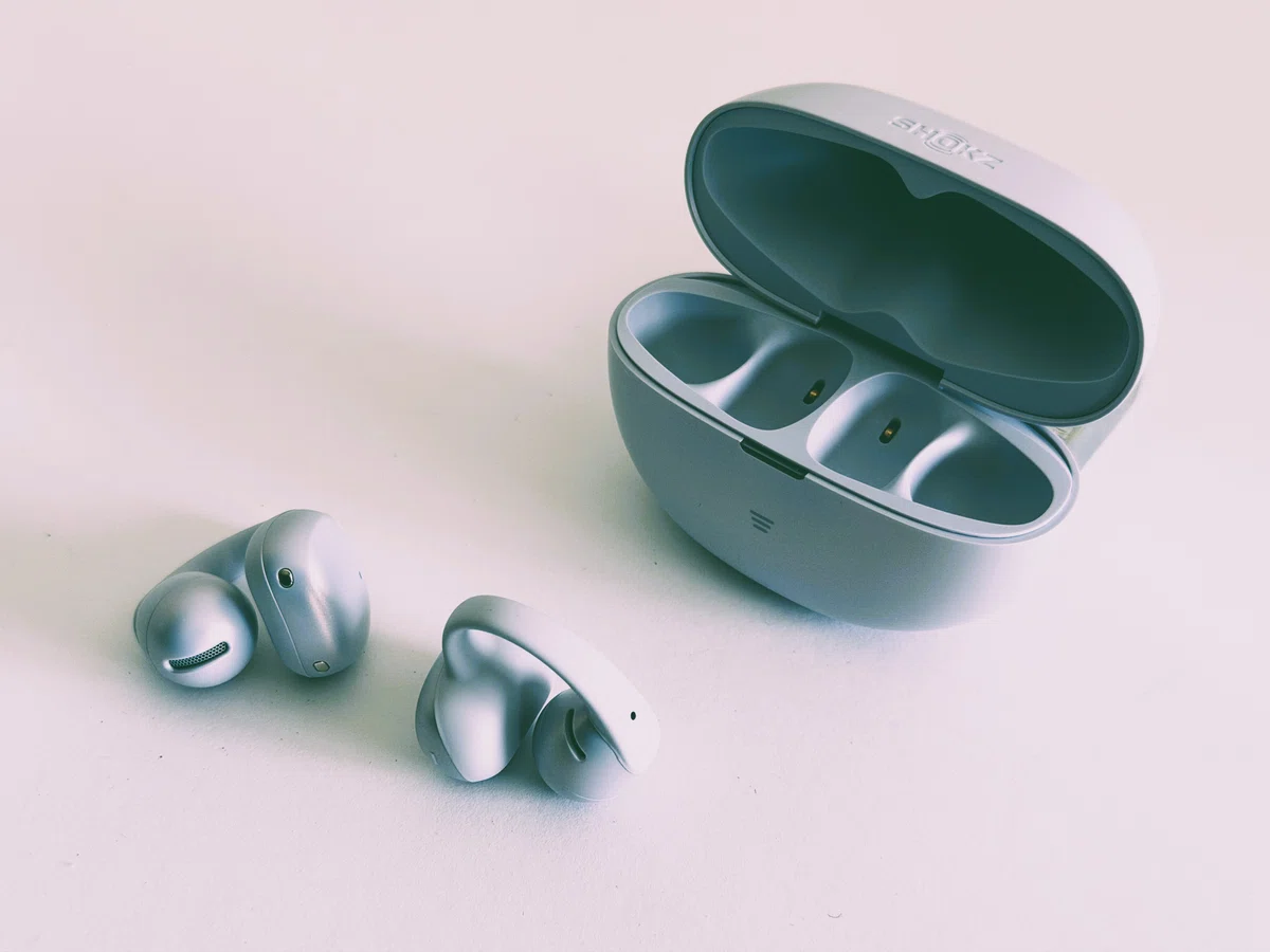 Shokz OpenDots Air デイブレイクパープル。耳に挟んで使うイヤーカフ型イヤホンとケースの外観写真。