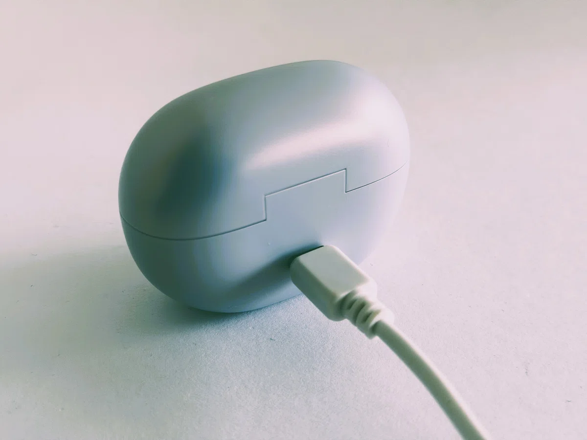 Shokz OpenDots Air デイブレイクパープル。耳に挟んで使うイヤーカフ型イヤホンのケースへUSB-Cを挿した充電状態。