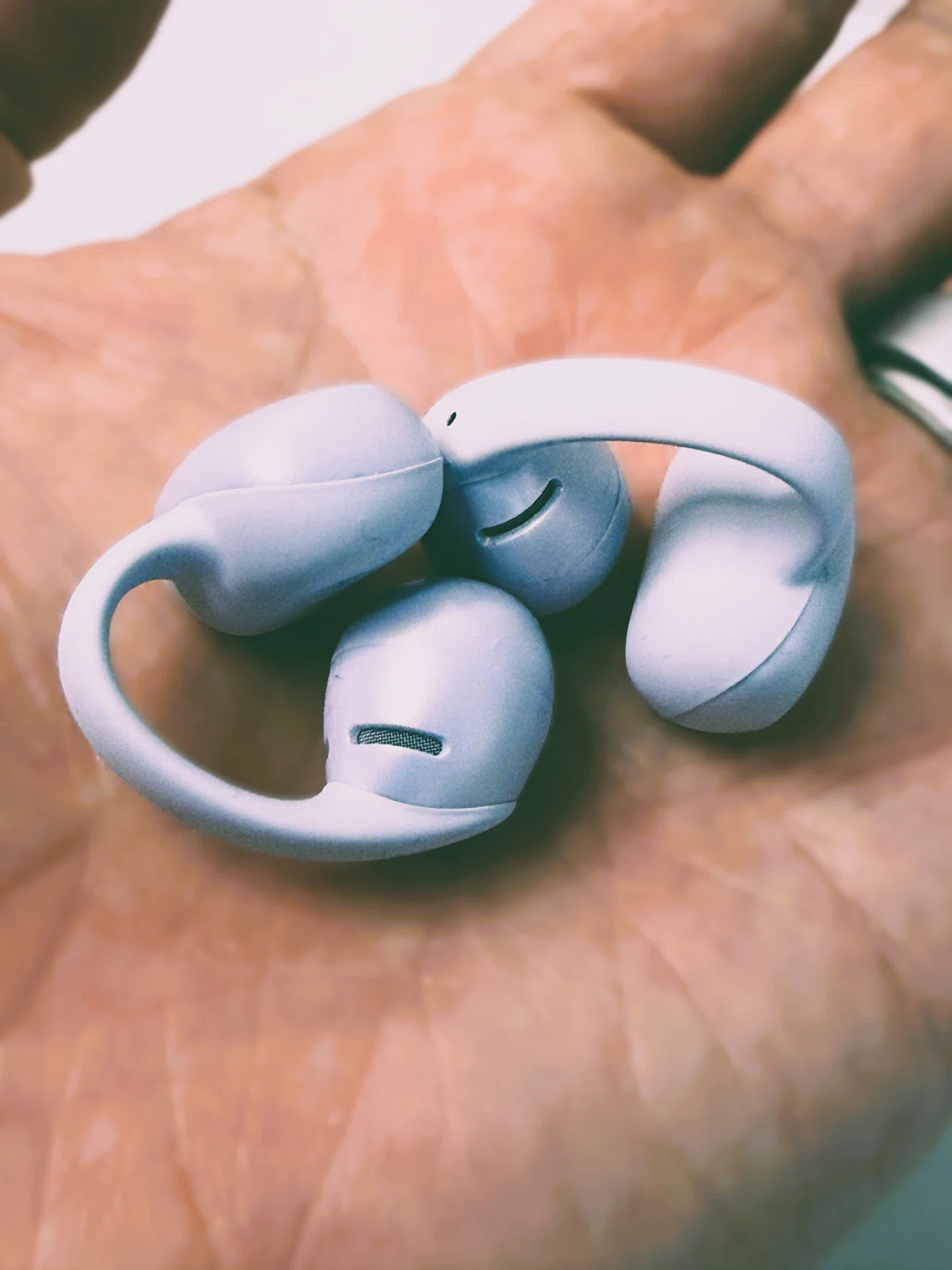 Shokz OpenDots Air デイブレイクパープル。耳に挟んで使うイヤーカフ型イヤホンを手のひらに載せた状態