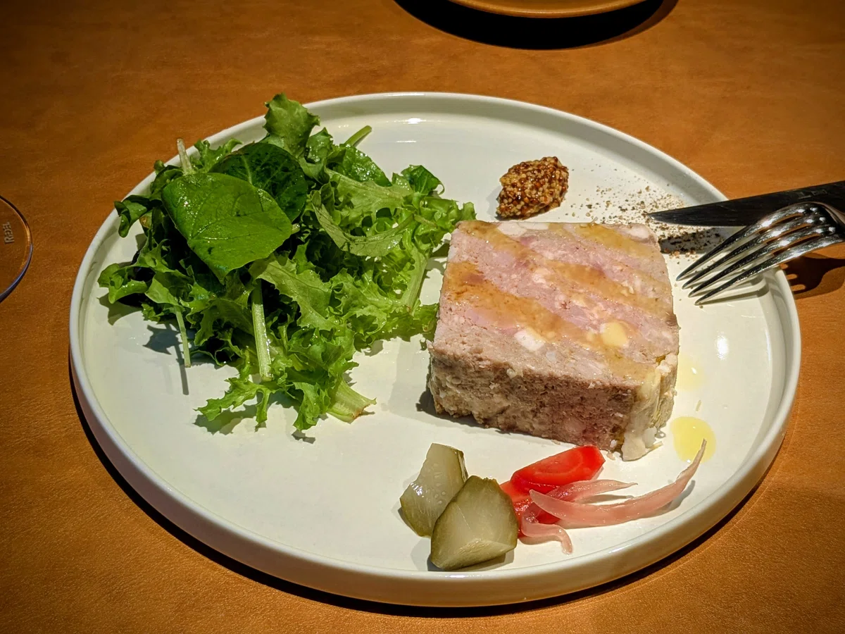 白い丸皿にパテ・ド・カンパーニュと葉野菜、ピクルス、マスタードが盛られている
