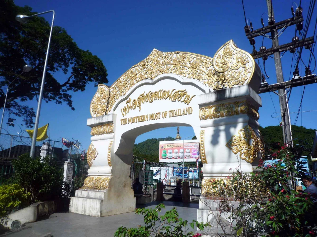 青空の下に、白と金色の装飾がある「THE NORTHERN MOST OF THAILAND」と書かれた門型の記念碑が立っている