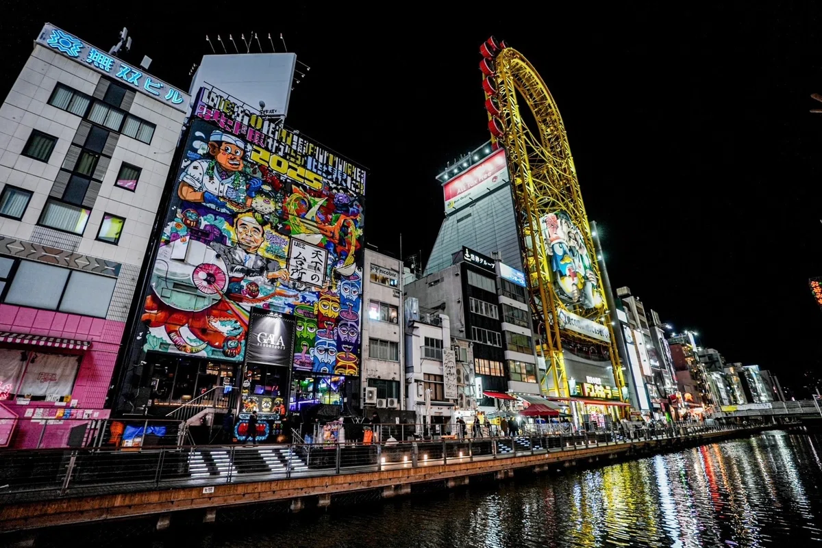 ightclub GALA RESORT along the Dotonbori Canal in Namba, Osaka, featuring its iconic colorful mural beside the Ebisu Tower Ferris wheel. A popular destination for Osaka nightlife, sightseeing, and international travelers exploring Dotonbori.