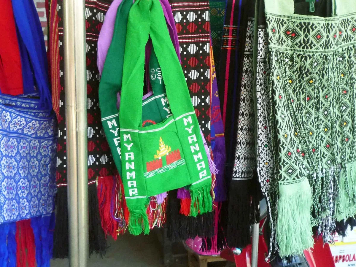 「MYANMAR」の文字と建物の模様が織られた緑色のバッグが、織物の間に掛けられている