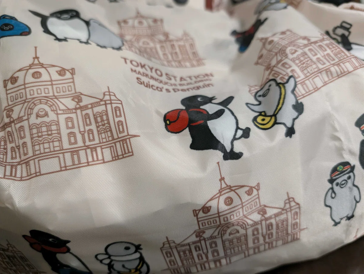 東京駅丸の内駅舎とSuicaのペンギンたちが描かれた総柄プリントのエコバッグ。お買い物やサブバッグに大活躍する日常便利グッズ Suicaのペンギンのエコバック@東京駅