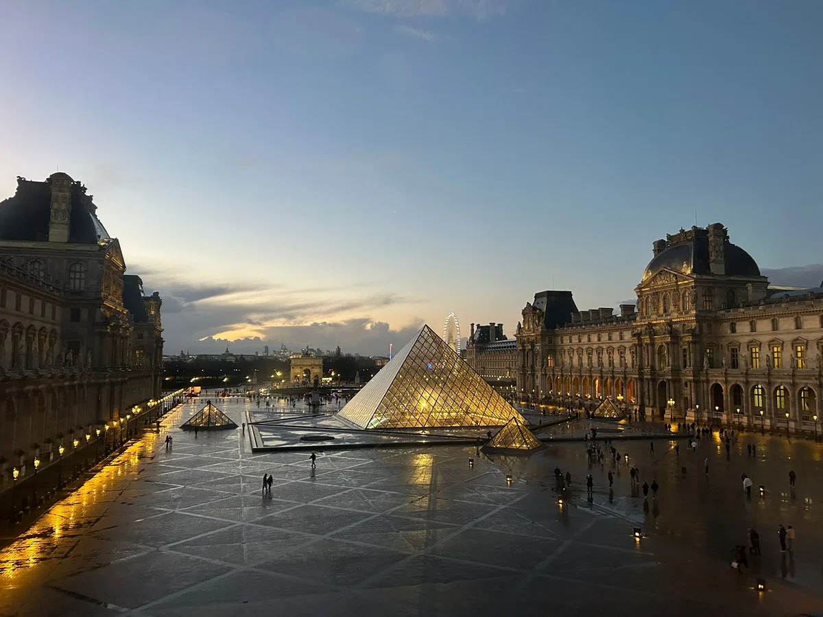 夕暮れのグラデーションの空の下、黄金色に美しくライトアップされたルーヴル美術館のガラスのピラミッドと広場の夜景。