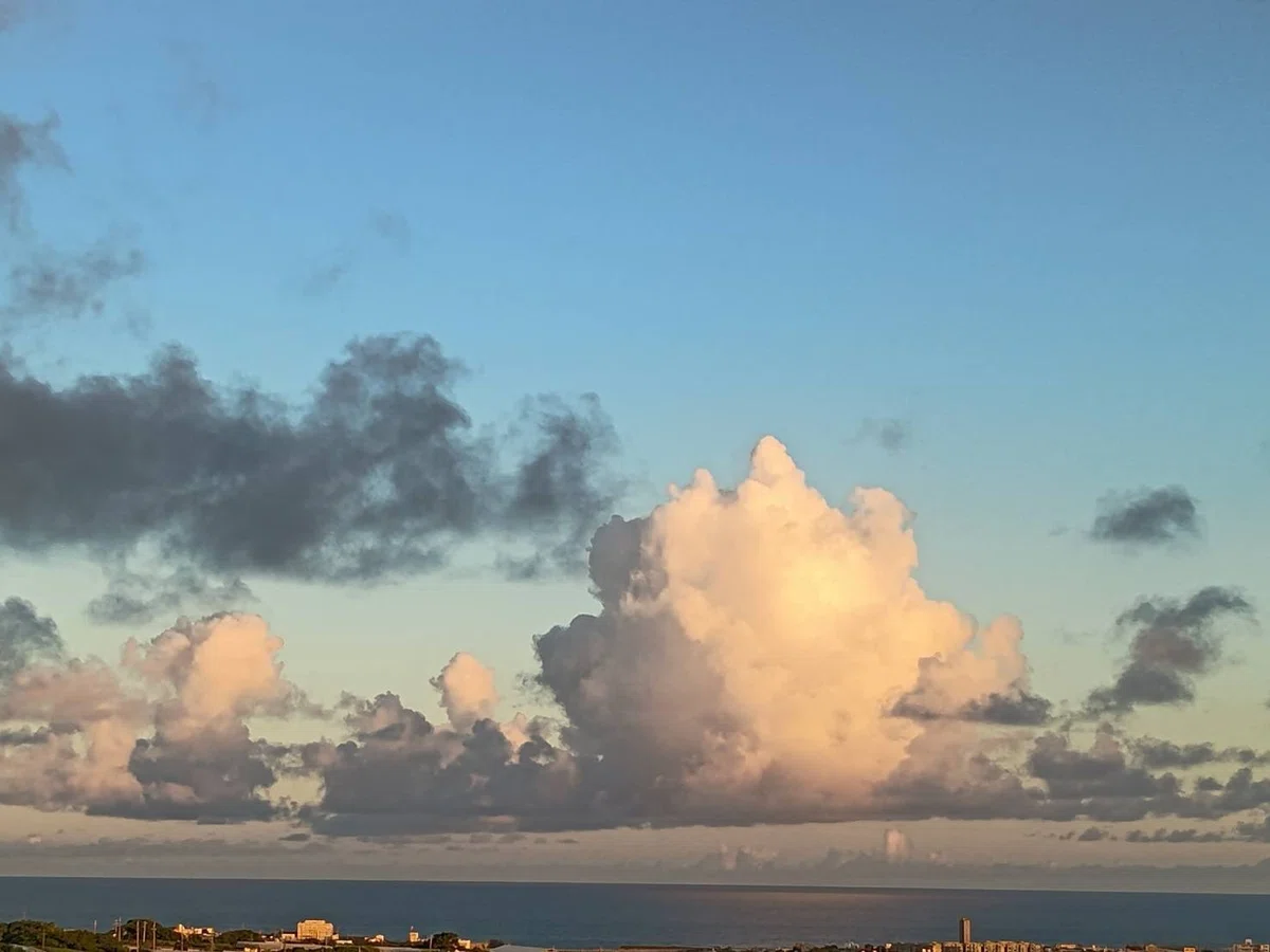 淡いオレンジ色とグレーのグラデーションの雲が浮かぶ夕方の青空、下の方に海