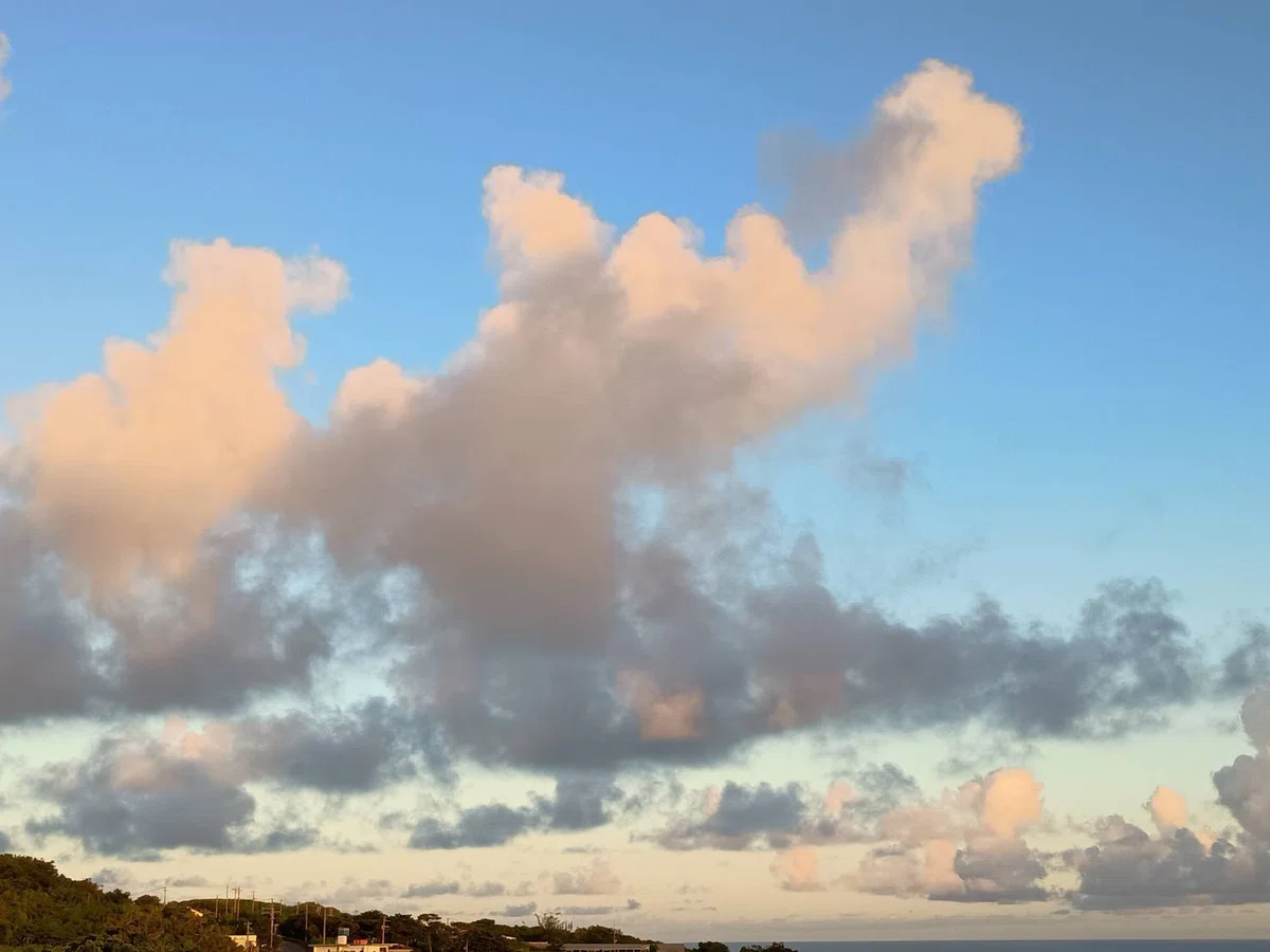 夕方の青空に浮かぶ、淡いオレンジ色とグレーのグラデーションの雲、下の方に山と海