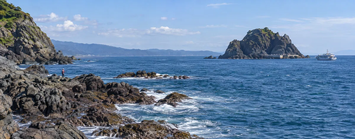 岩礁が続く海岸で釣り人が磯釣りをする風景