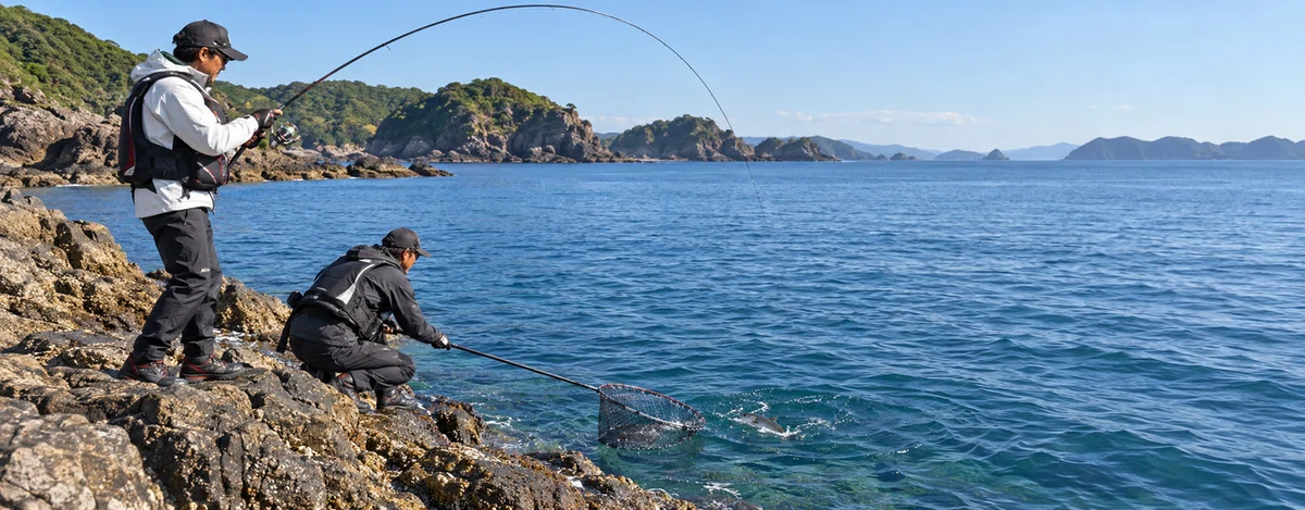 岩礁の魚を竿で寄せて取り込む磯釣りの場面