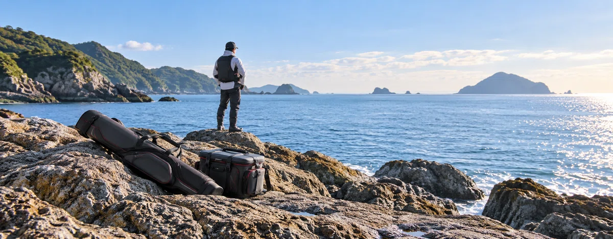 休日の海を眺める釣り人と磯の道具