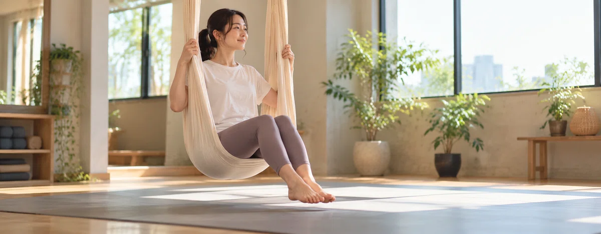 吊り布に座り、足を床から少し離して両手で布を持つ参加者