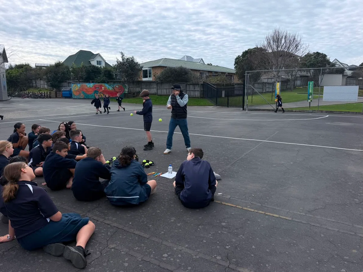 Children seated outdoors at Gulf Harbour School as an adult demonstrates an activity on the school grounds.