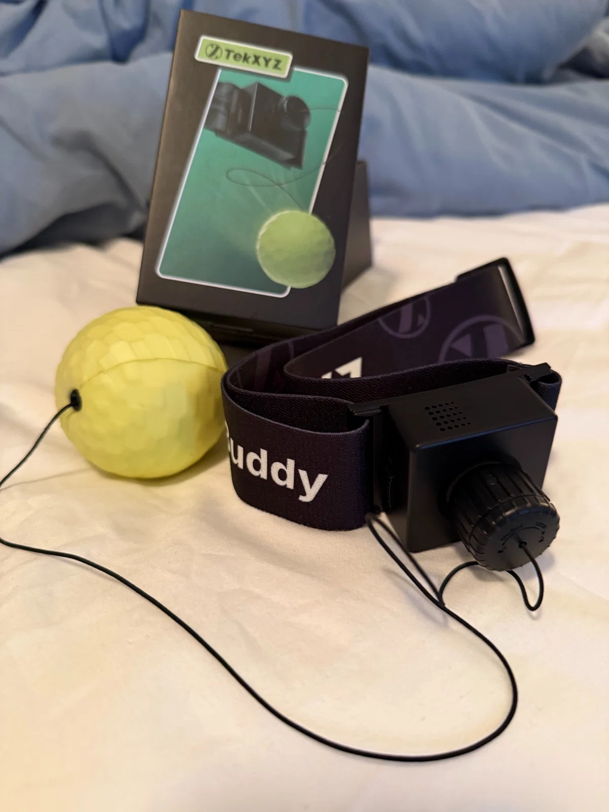 A yellow boxing reflex ball with a black headband and packaging, photographed on a bed.