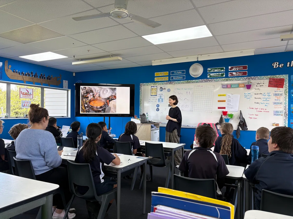 A classroom presentation showing a photograph of a Japanese school lunch kitchen on a screen.