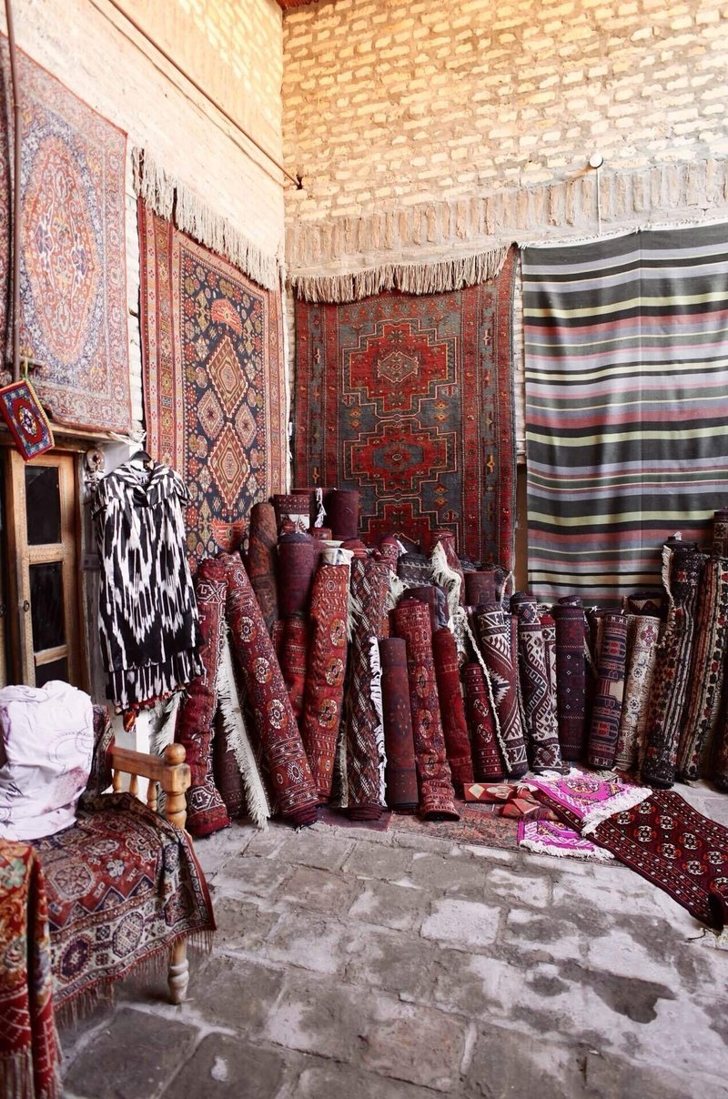 レンガ造りの壁に飾られた絨毯と、その前に丸めた状態で並べられたたくさんの絨毯