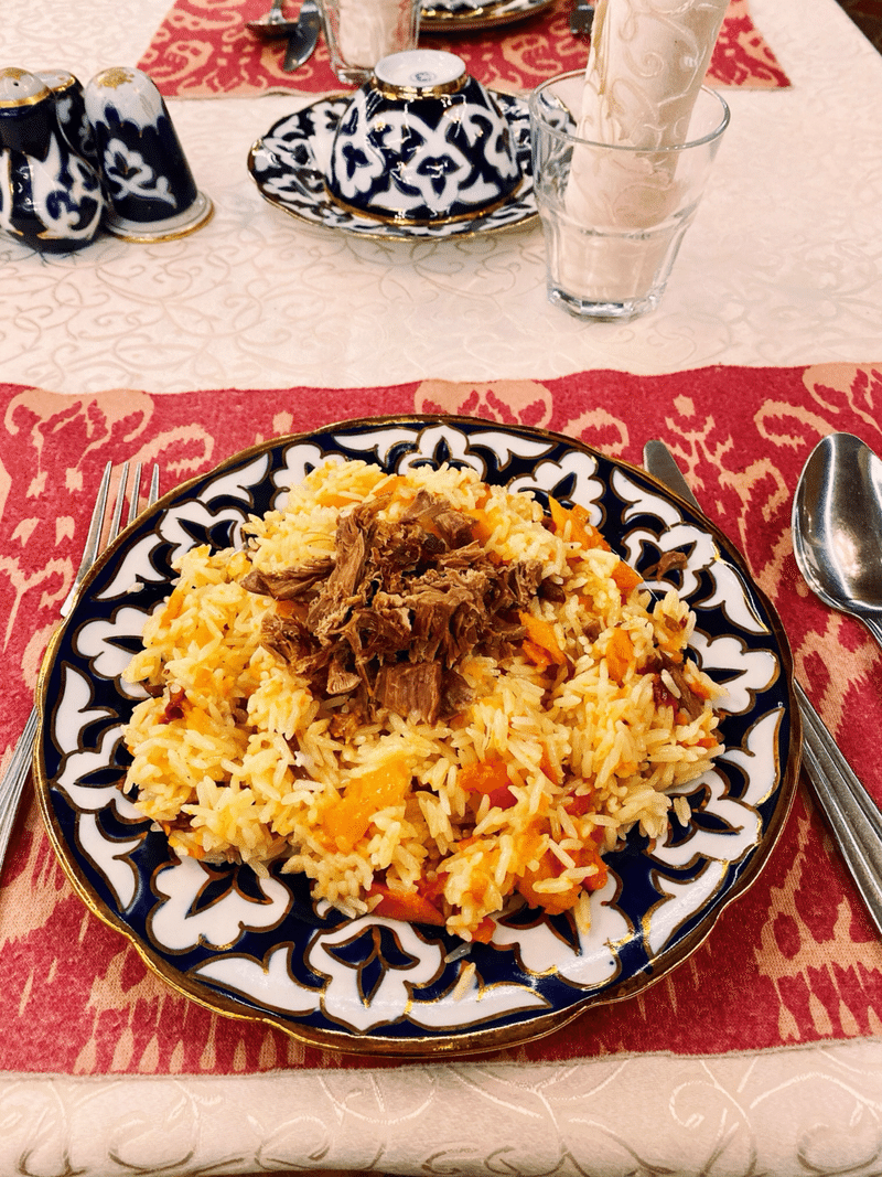テーブルクロスの上に置かれた米料理。炒められた黄色い米には、カットされ炒められたニンジンが混ざっている。米の上にはほぐされた肉が乗っている