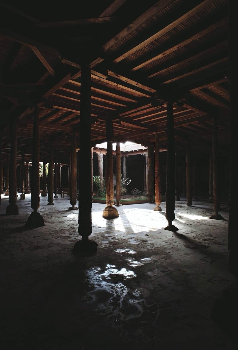 複数の木製の柱が並ぶモスク内部の様子。全体的に暗いが、中央は天井があいており、外からの光が差し込んでいる
