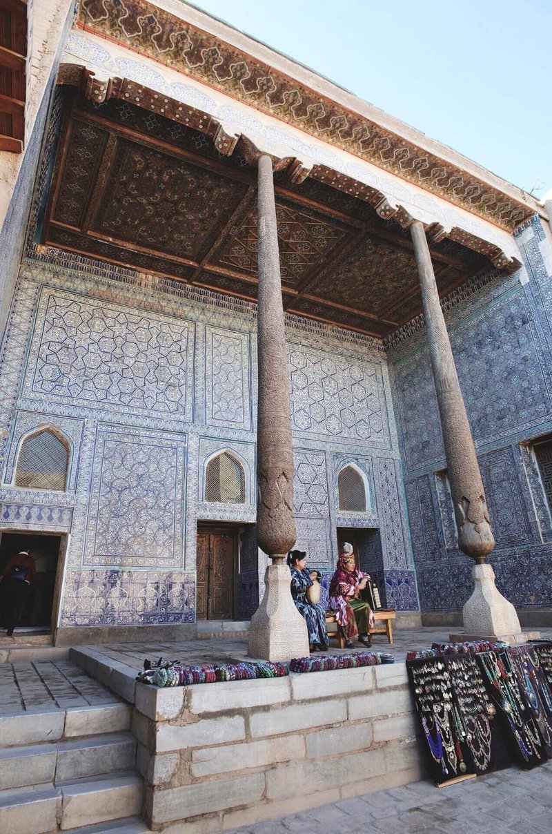 アラベスク模様のタイルで覆われた建物の中で、女性二人が演奏している。その前には毛糸の靴下やアクセサリーなどのお土産が並べられている
