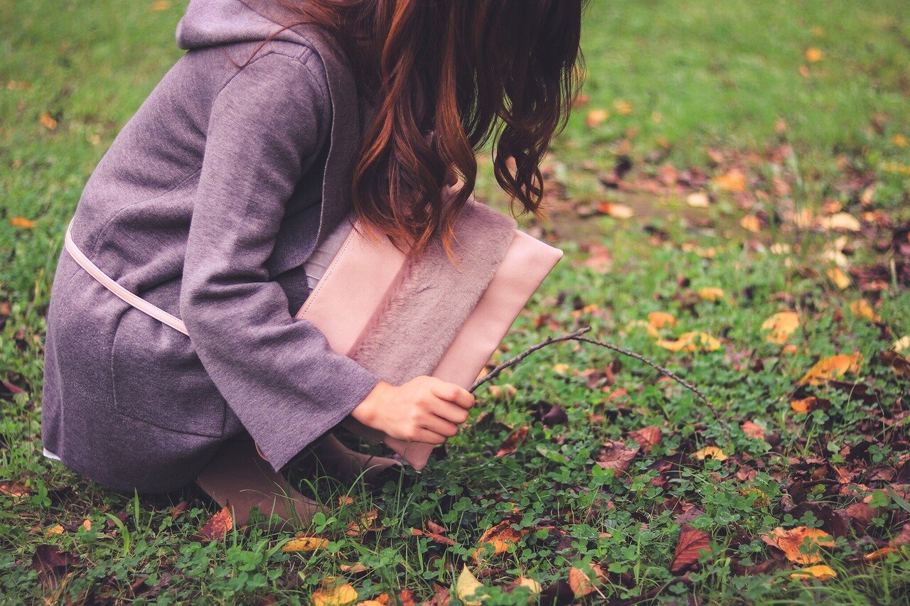 木の枝で秋のカラフルな地面をツンツンする女の子