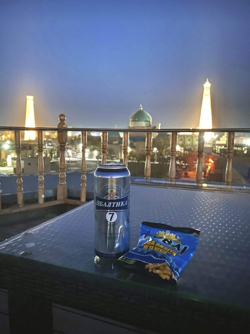 ホテルの屋上からライトアップされた街並みを眺める様子。手前のテーブルには、缶ビールとスナック菓子が置かれている