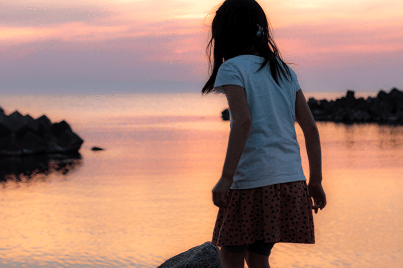 夕暮れの海辺で、茜色の夕焼けに染る綺麗な海に感動して涙を零した女の子。