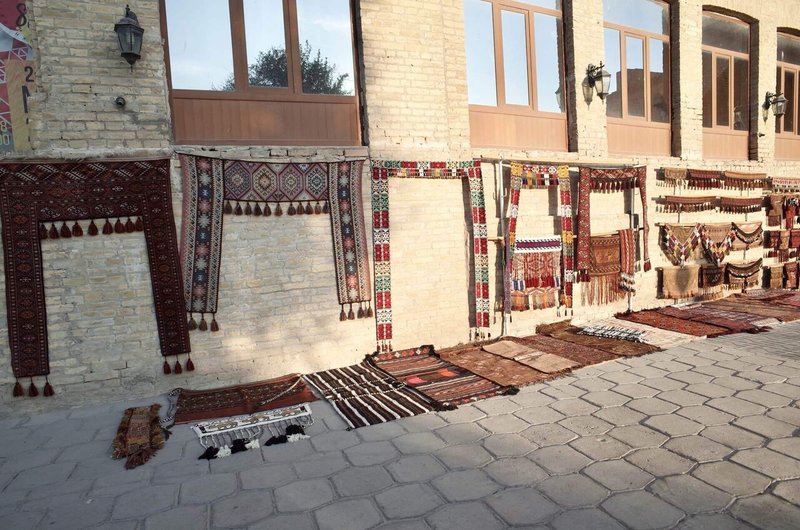 屋外の壁と道に、さまざな柄で織られた飾り布や絨毯が置かれている様子