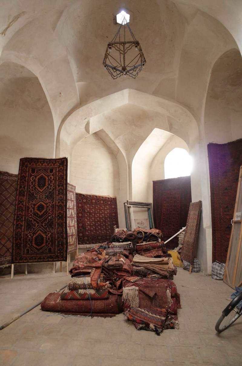 ドーム状の天井の建物の中。床には古い絨毯がたくさん重ねられ、壁にも絨毯が置かれている様子