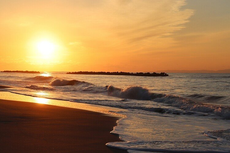 白波が次々と足元に押し寄せる。波が引いた濡れた砂浜は鏡のように夕陽の光を映し出す