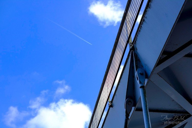 青い空に青い歩道橋、そこへ一筋の飛行機雲。