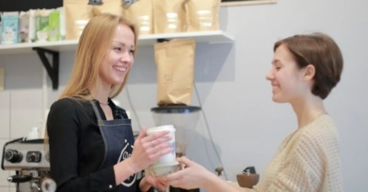 カフェ店員の女性が女性客にコーヒーを渡す様子
