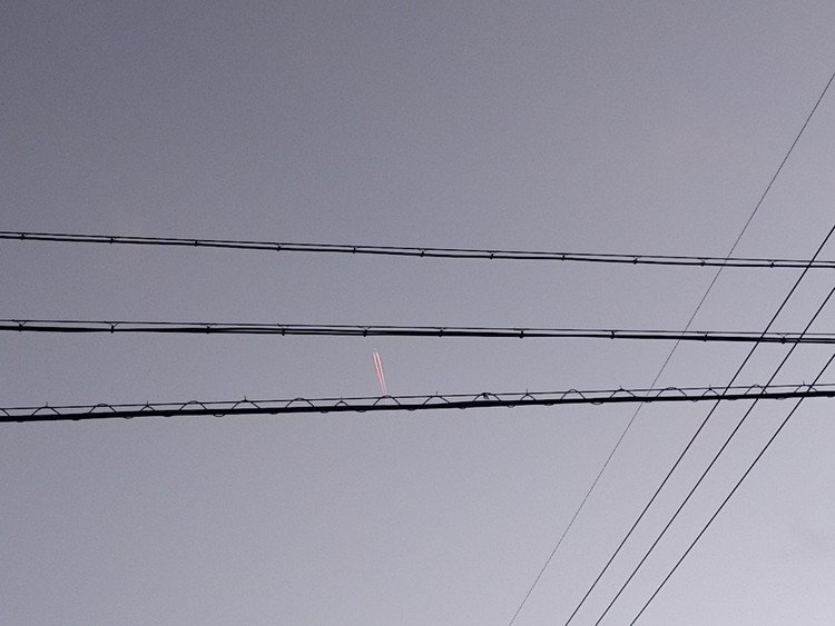 ふと見上げた今日の夕方の空。

電線の隙間を飛ぶ、飛行機雲。いや、飛んでいるのは飛行機か。
航跡が夕陽を浴びてかすかに赤い。