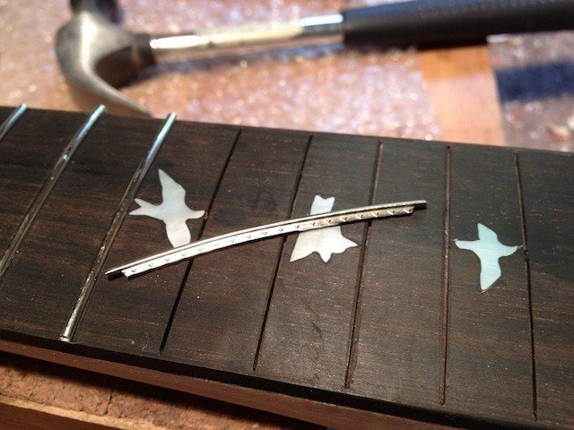 フレットを打ちます。フレットは事前に必要な長さに切り、指板のRよりも少しキツいR上に曲げておきます。このギターの場合は指板の両サイドに1.5mmの木が貼られているので、それを避けるようにフレットを削っています。