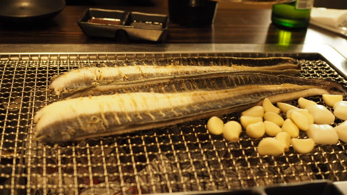 網の上に開かれた鰻とたくさんのにんにく