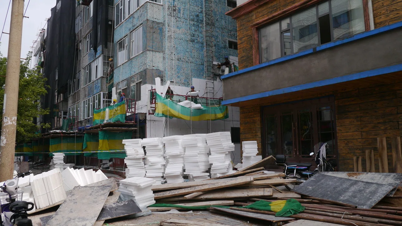 中国で住宅を買うのをためらう風景 古いビルに貼り付けられている白い物は発泡スチロールだ レンガ作りのビルにセメントを塗り その上から発泡スチロールをはり ネットで覆ったあと またセメントで固める 映画の Meguru Ishida Note