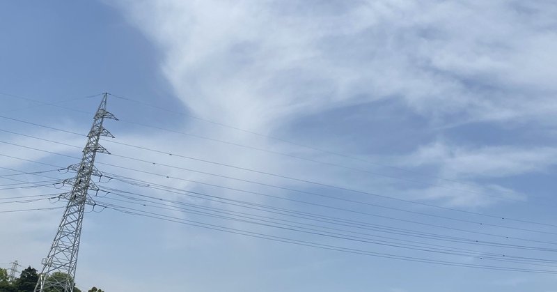 白くて薄い雲がかかった空をバックに立つ鉄塔と電線の写真
