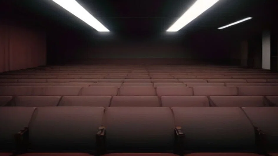 映画館の客席を後ろの列から見たところ。赤い座席が奥の暗がりまで並び、天井の細長い照明だけが光っている。人はいない