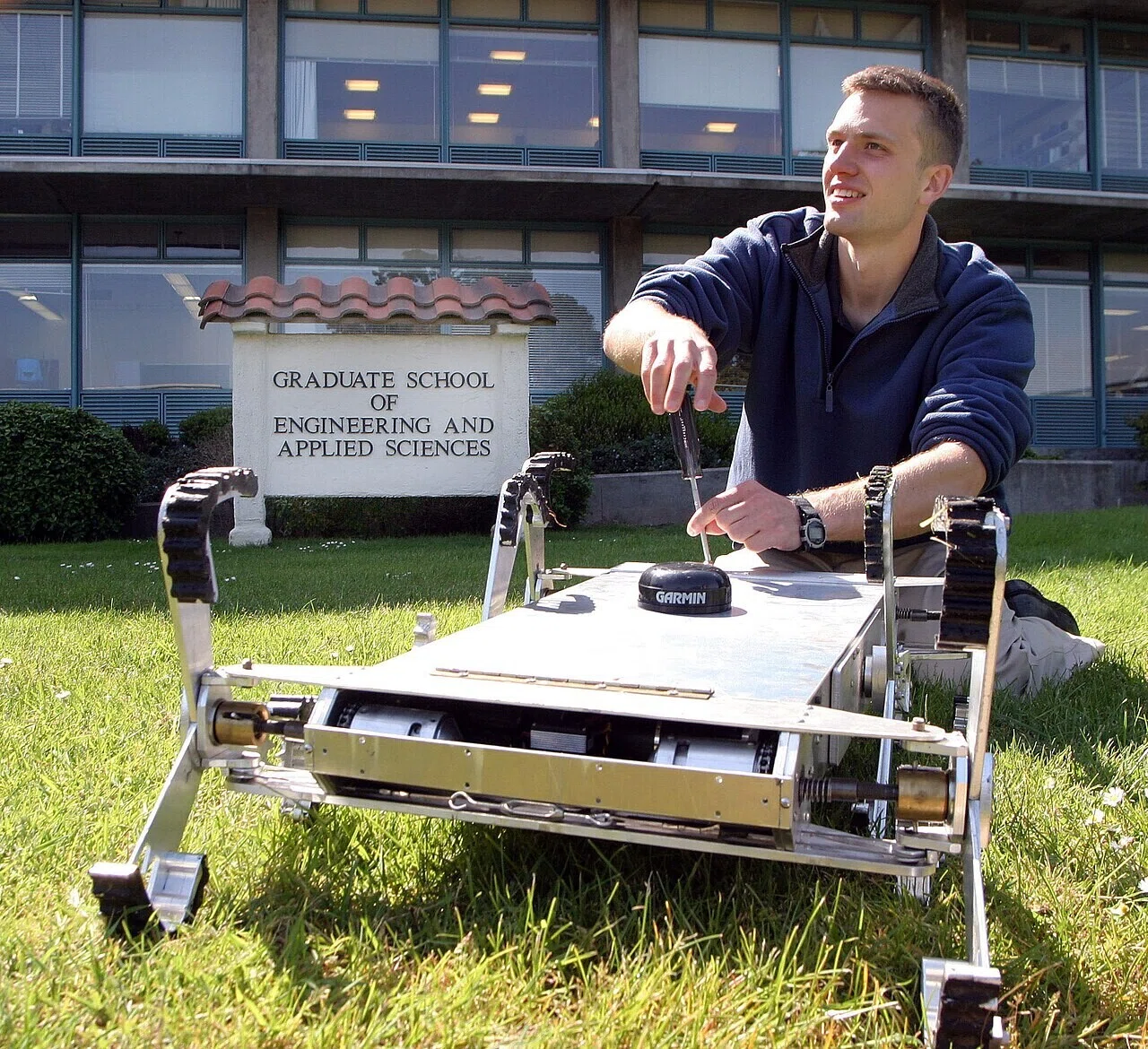 屋外で不整地走行式の自律型ロボットを調整する担当者の姿。農業を想定して設計された機械を人が手で仕上げる場面が、AI任せにしない実践の大切さを物語る。