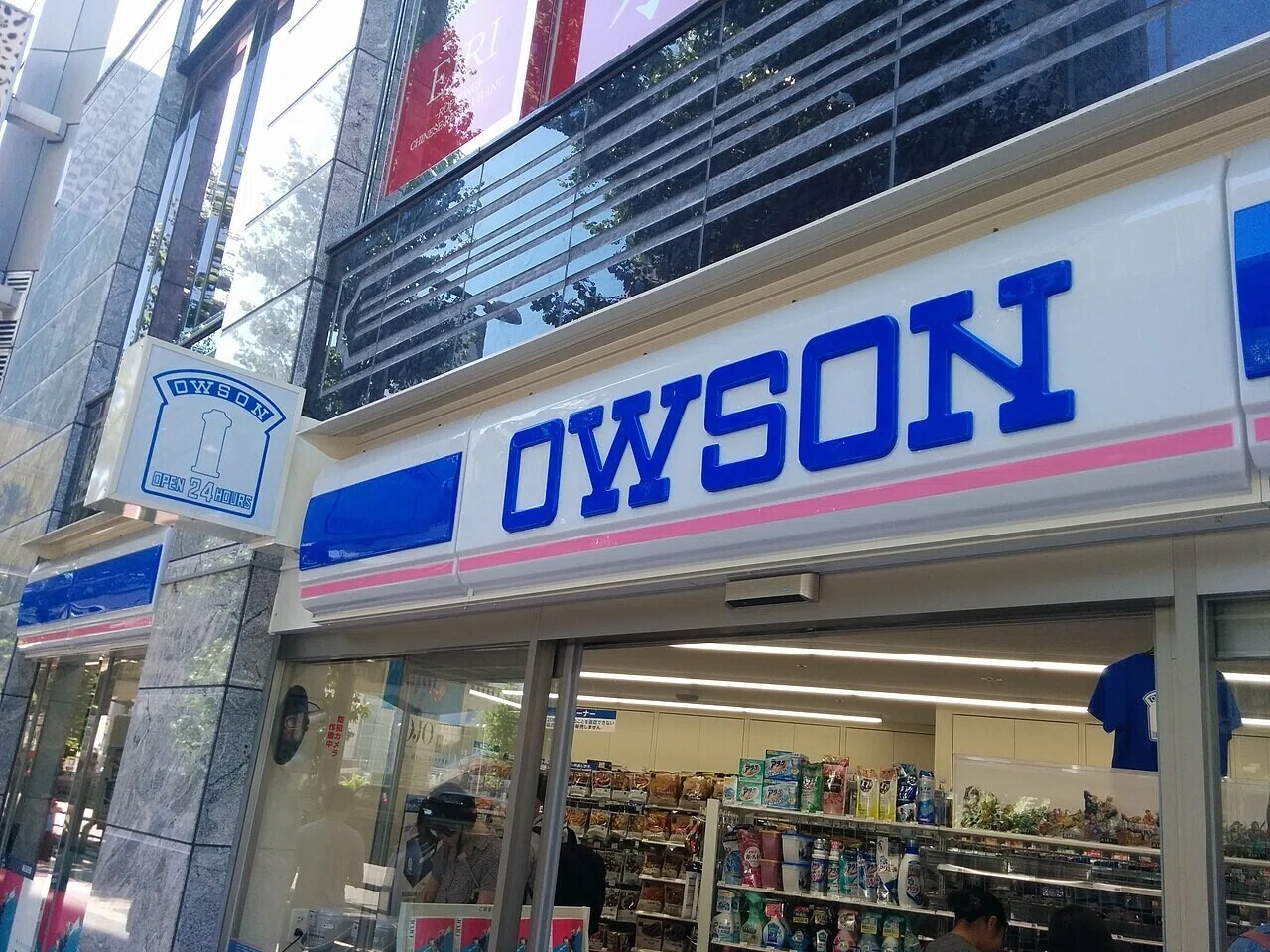 ガラス越しに明るい店内がのぞくコンビニの外観。夜でも眠らない店という古代の選択を、後世の読者への手がかりとして示す一枚だ。