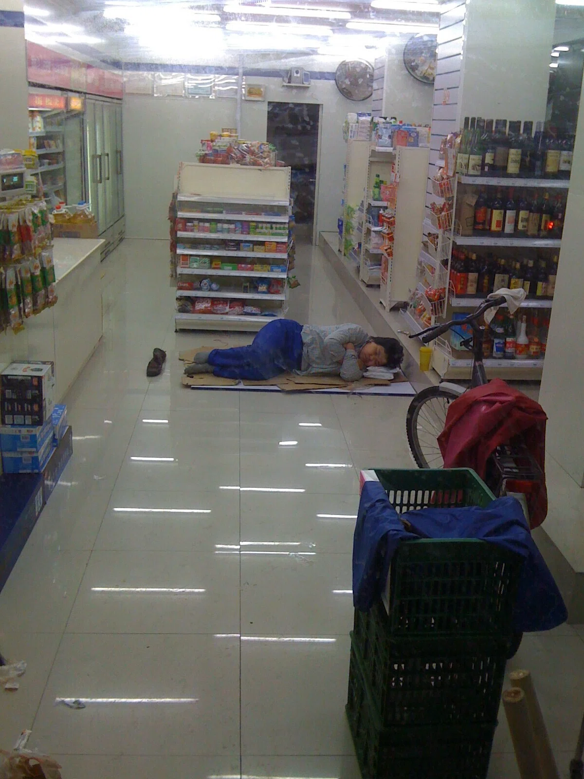深夜の店内で段ボールの上に横たわる人物。眠らないはずの店の夜に潜む、見えにくかった営業の実態を垣間見せる。