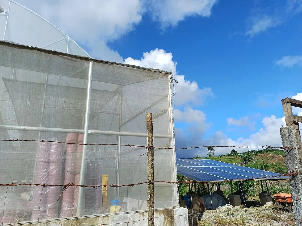 ソーラーパネルを備えたネット張りの温室が畑の傍らに建つ、太陽光発電による水耕栽培システムの様子。次節で扱う養液供給の仕組みを身近な規模で示す一例といえる。