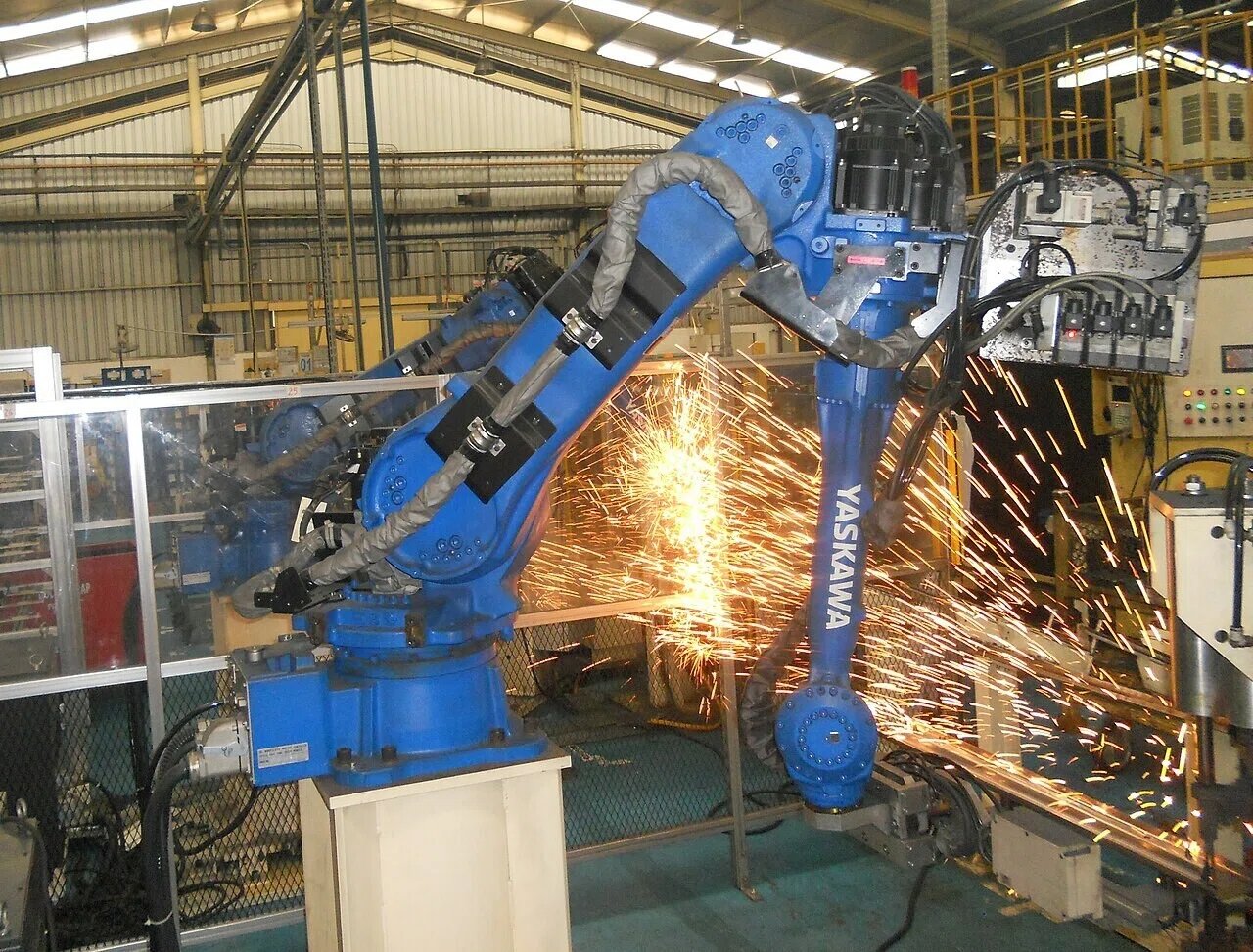 火花を散らして溶接作業を行う産業用ロボットアーム。従来型の「繰り返し精度」に頼る溶接の姿が、次節で語る市場の勢力図の前提となる。