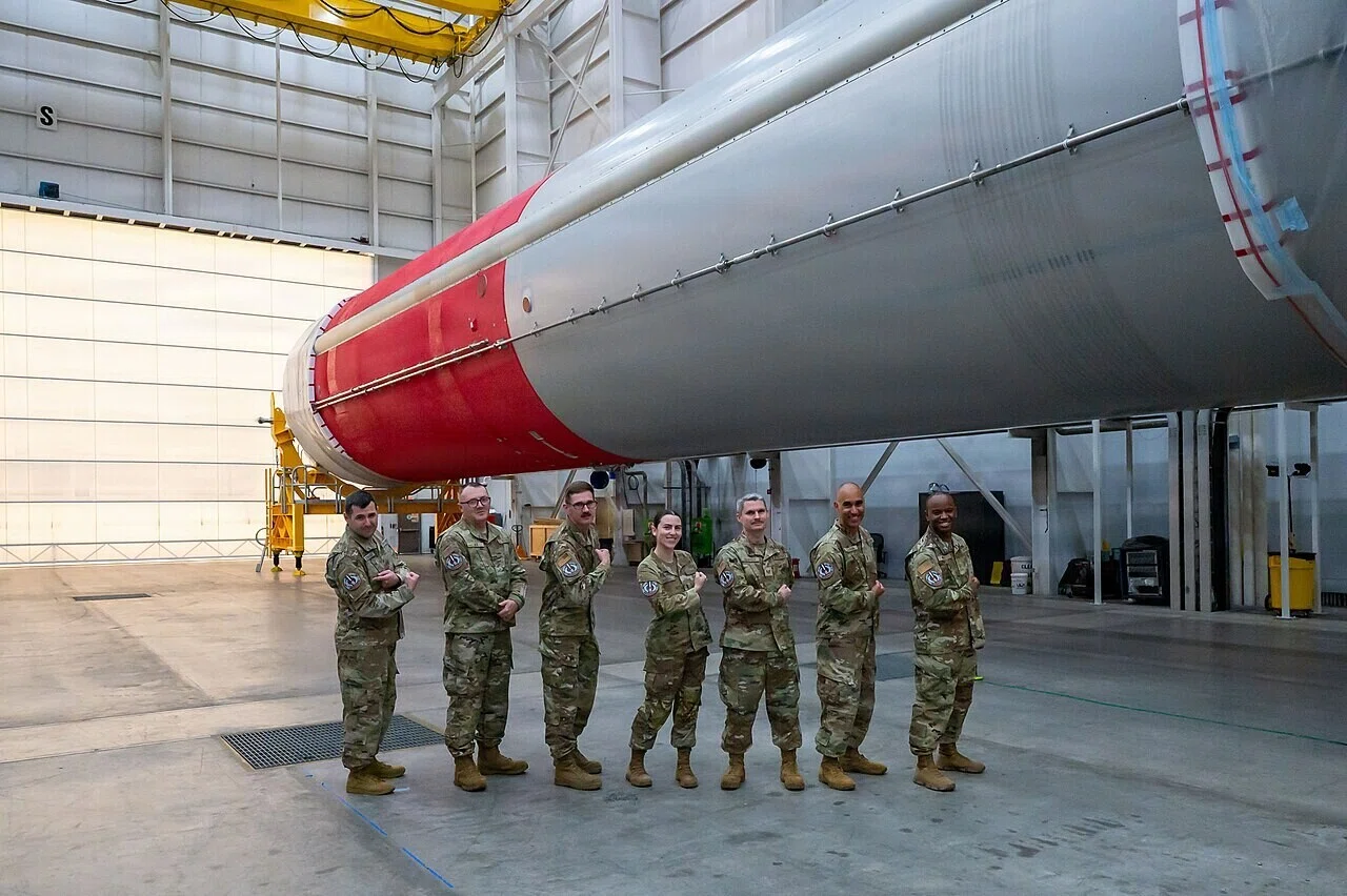 ハンガー内で大型ロケットの前に並ぶ制服姿の米宇宙軍関係者。軍と民の打ち上げ体制の連携を示す一場面です。