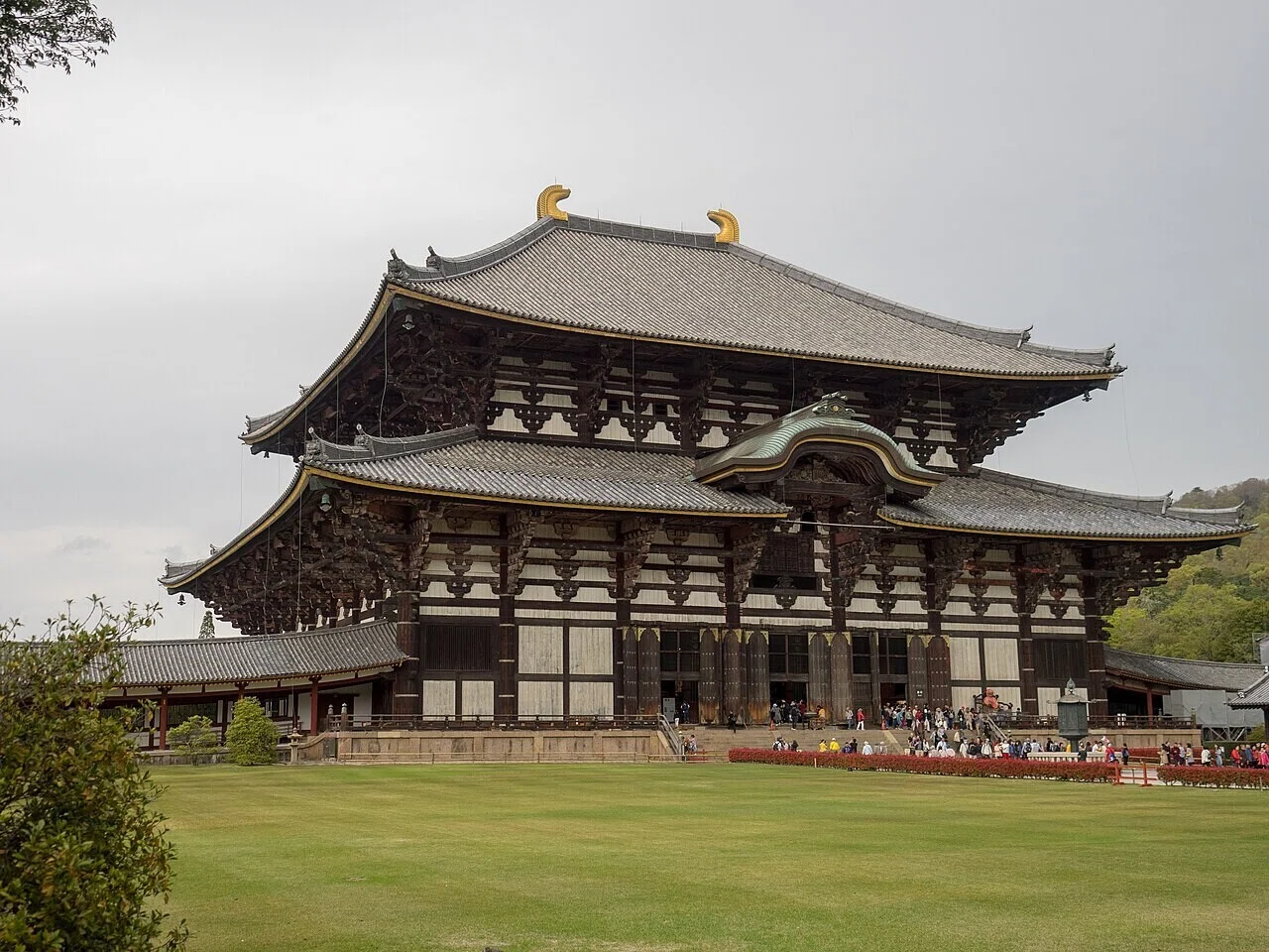 芝生の向こうに建つ東大寺の大仏殿と、石段に集う来訪者たち。秋晴れの下で人々が訪れる様子が、快適なお出かけ日和を示す。