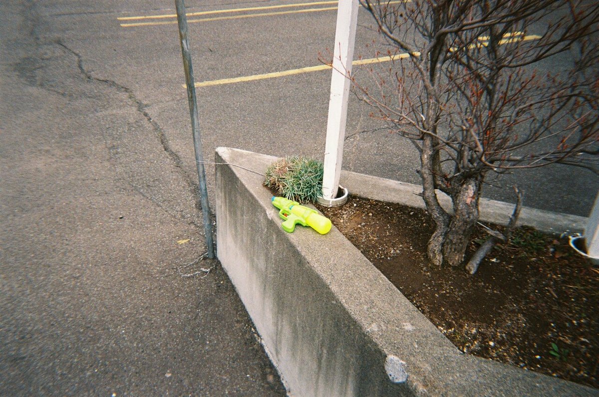 花壇の縁に置かれた水鉄砲のフィルム写真。