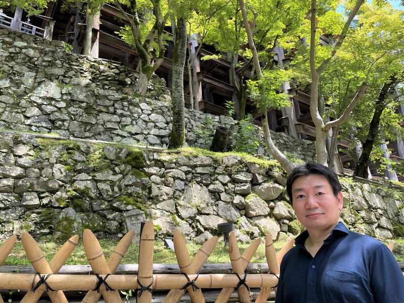 京都にある清水寺の「清水の舞台」の真下にある、石垣の前に立つ内閣官房IT総合戦略室の本丸達也IT戦略調整官。