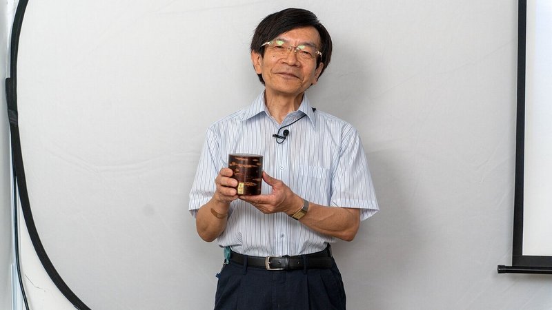 嶋村吉洋氏主催ワクセル講演会：説明に用いた茶筒を持つ石井氏の写真
