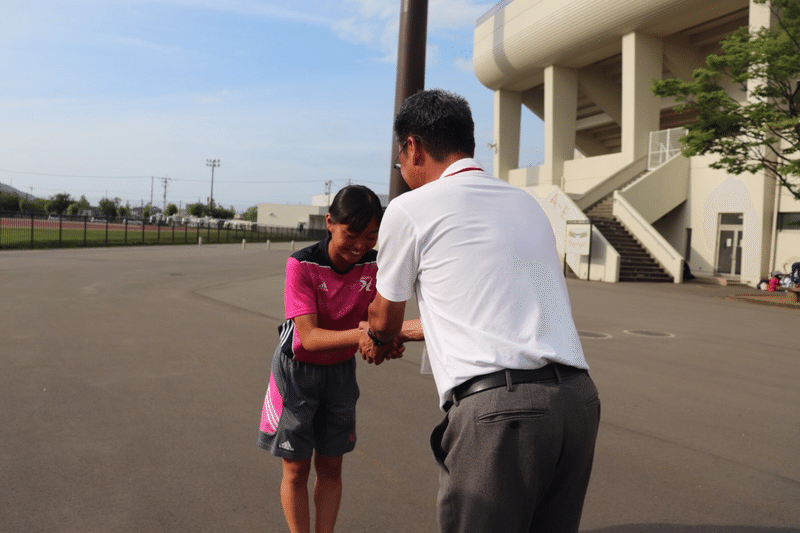 笑顔で握手を交わす矢尾さん(左)と顧問の吉田良一先生(右)